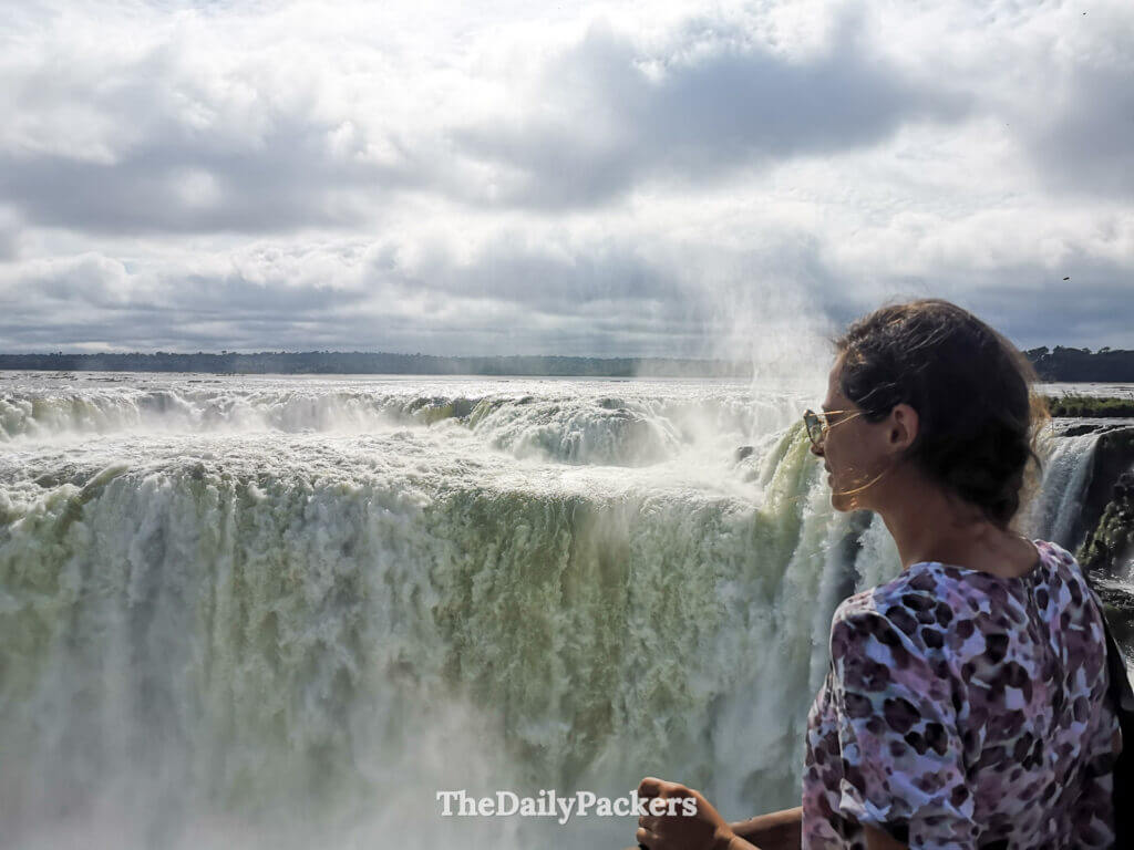Woman standing at Devil’s Throat viewpoint overlooking Iguazu Falls and mist