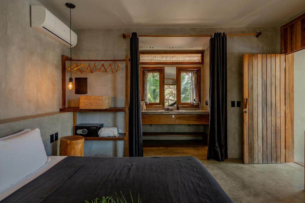 Modern tropical hotel room at Villa Mango Jeri with concrete finishes, wooden furniture, and open-plan bathroom in Jericoacoara
