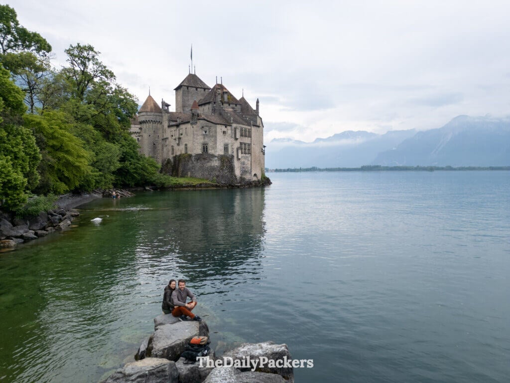 Couple sitting by the water with Chillon Castle rising from Lake Geneva behind