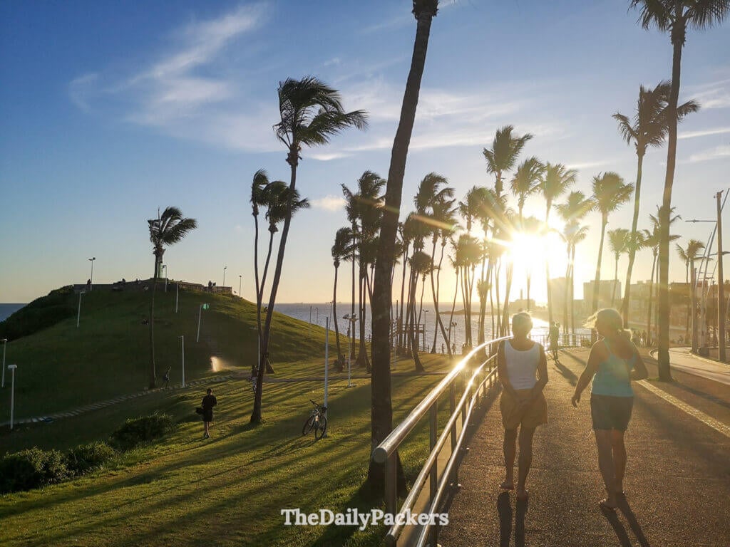 Sunset walk near Morro do Cristo in Salvador with palm trees, ocean views, and locals enjoying the coastal promenade