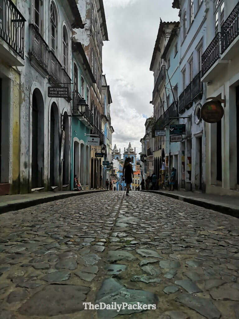 Low-angle view of a cobblestone street in Pelourinho, Salvador, with a traveler walking toward colorful historic houses