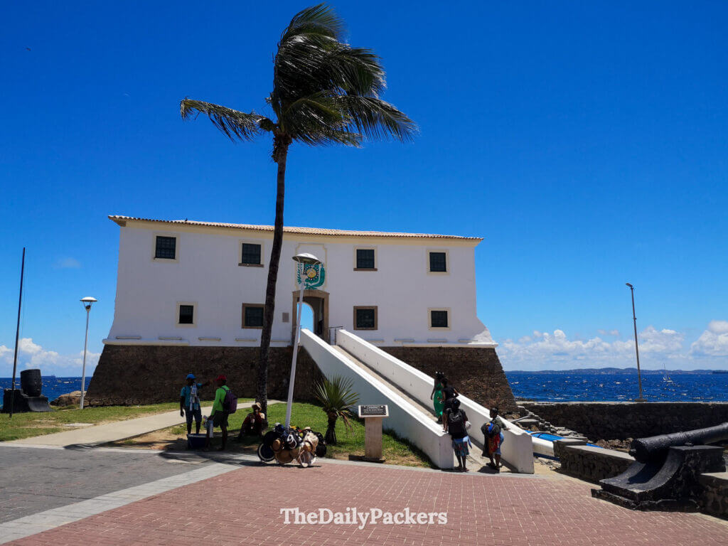 Forte São Diogo in Salvador with white walls, palm tree, and visitors exploring the historic seaside fort