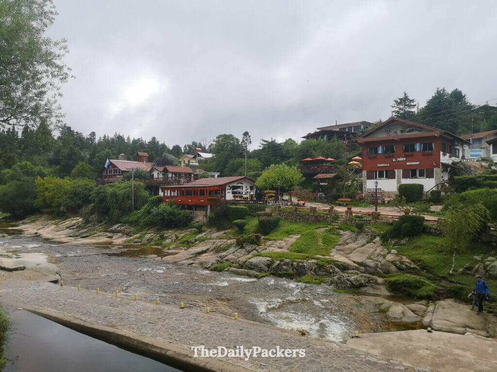 Paysage de village au bord de la rivière à La Cumbrecita, avec des maisons et des collines verdoyantes