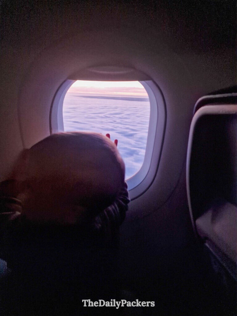 Nourrisson regardant par le hublot de l'avion le ciel bleu éclatant et les nuages pendant le vol.