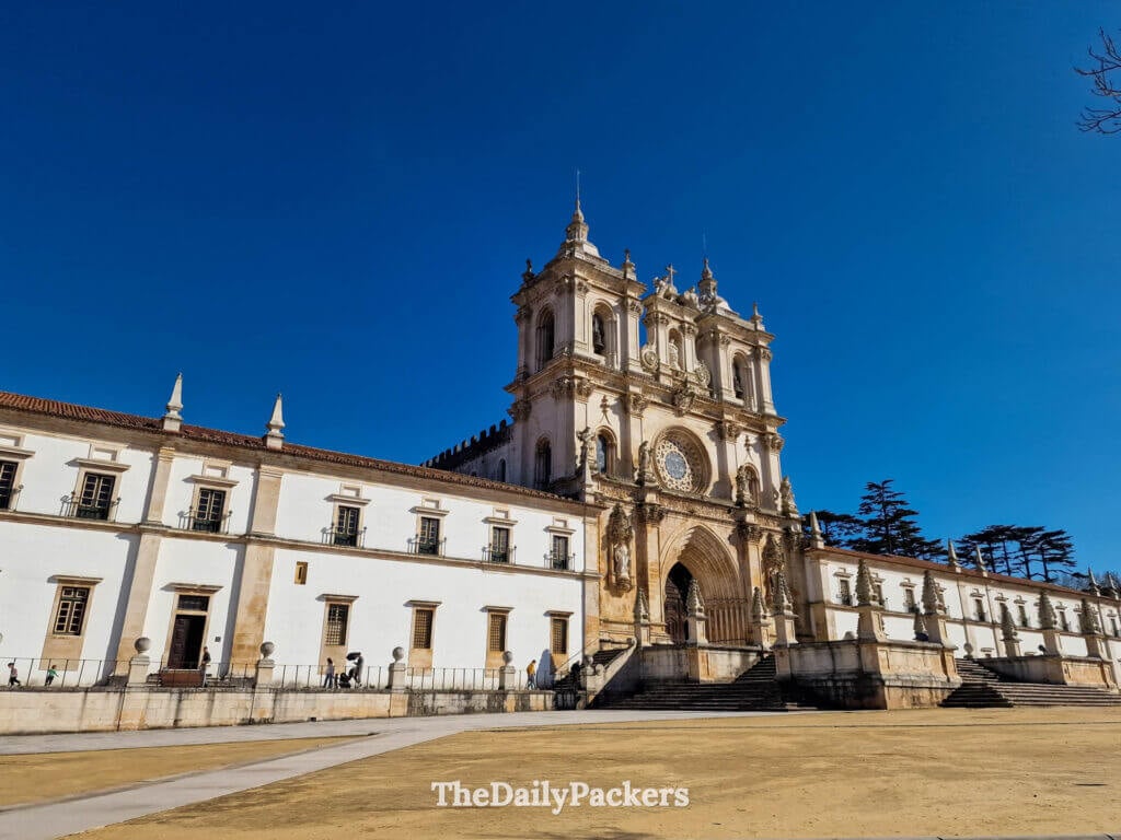 Vue extérieure de la façade du monastère gothique d'Alcobaça sous un ciel bleu limpide au Portugal.