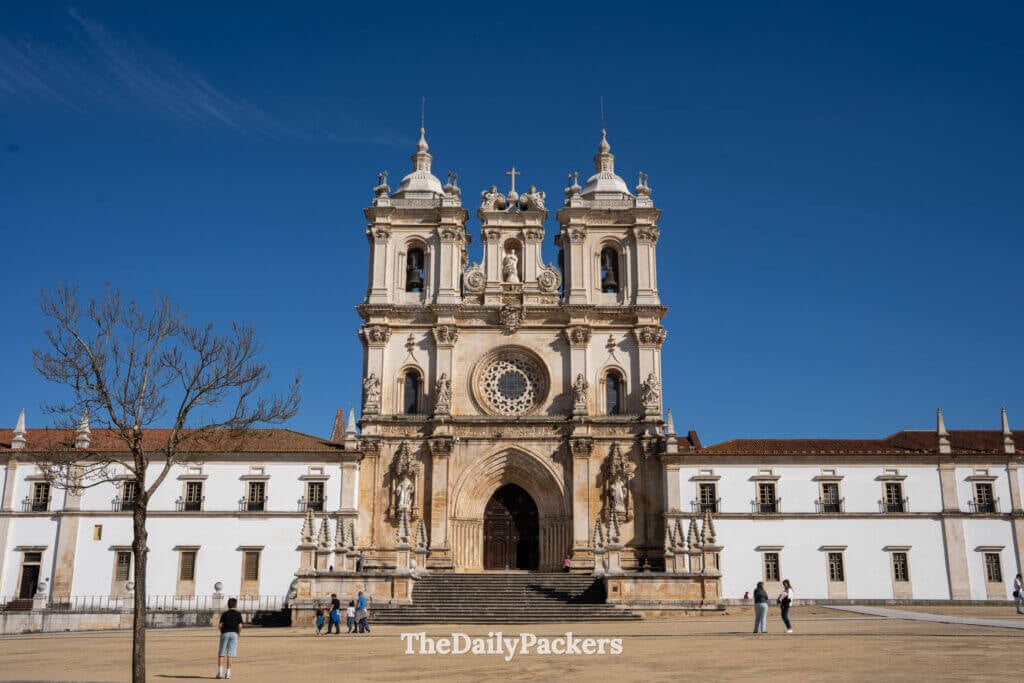 Vue large de la façade du monastère d’Alcobaça avec ses longues blanches ailes et son église centrale.