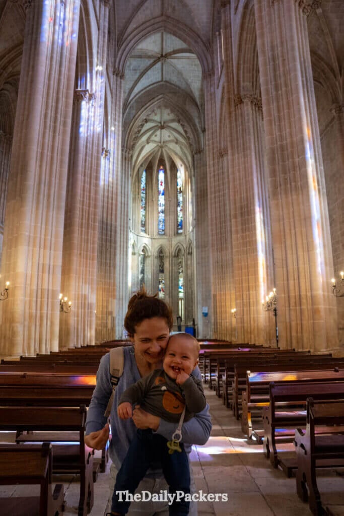 Une personne tenant un jeune enfant à l'intérieur de la grande nef faiblement éclairée du monastère de Batalha.