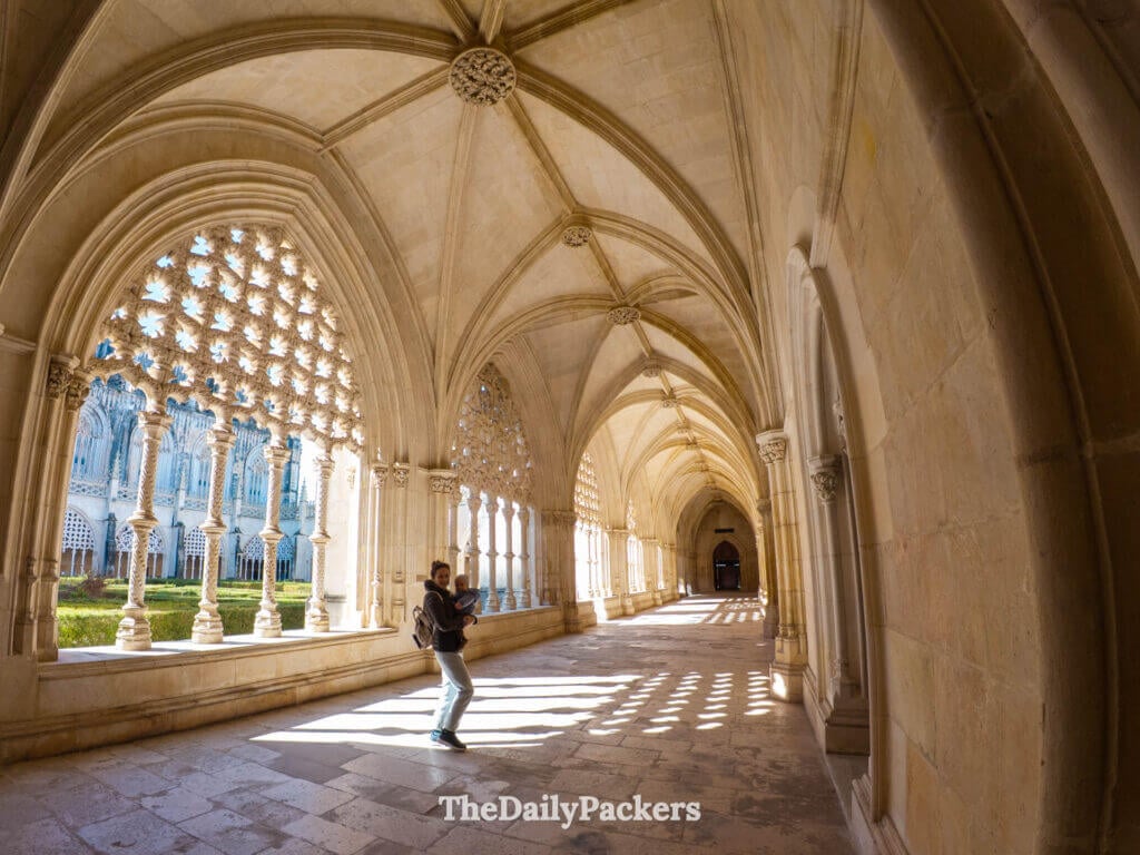 Femme tenant un bébé dans le couloir gothique ensoleillé du cloître royal au monastère de Batalha.