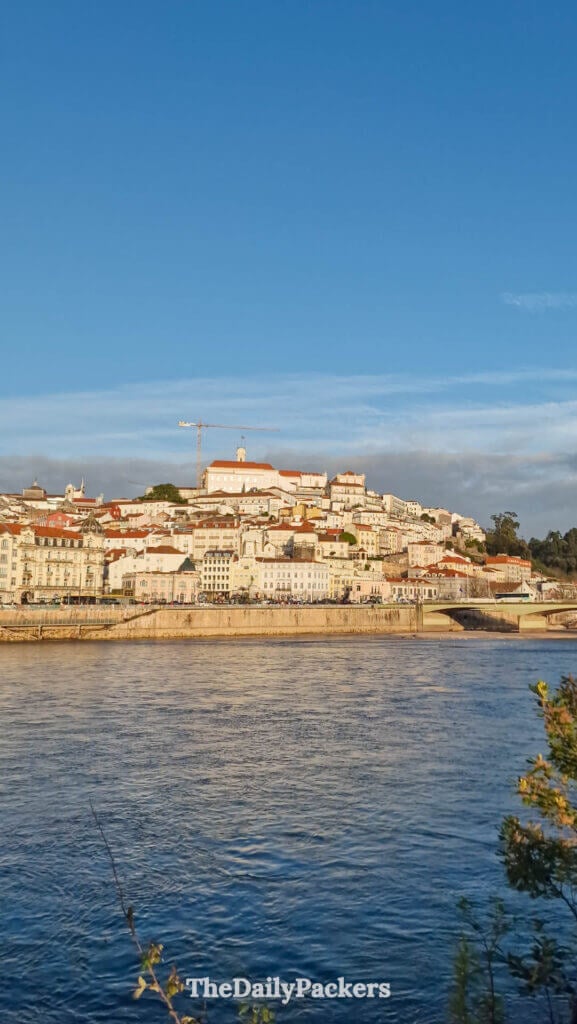 Photo verticale des bâtiments colorés du front de rivière de Coimbra et de la tour de l’université, au bord du Mondego.