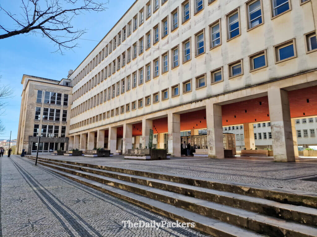 Extérieur du bâtiment de la billetterie de l'université de Coimbra avec des piliers modernes et une place en pierre.