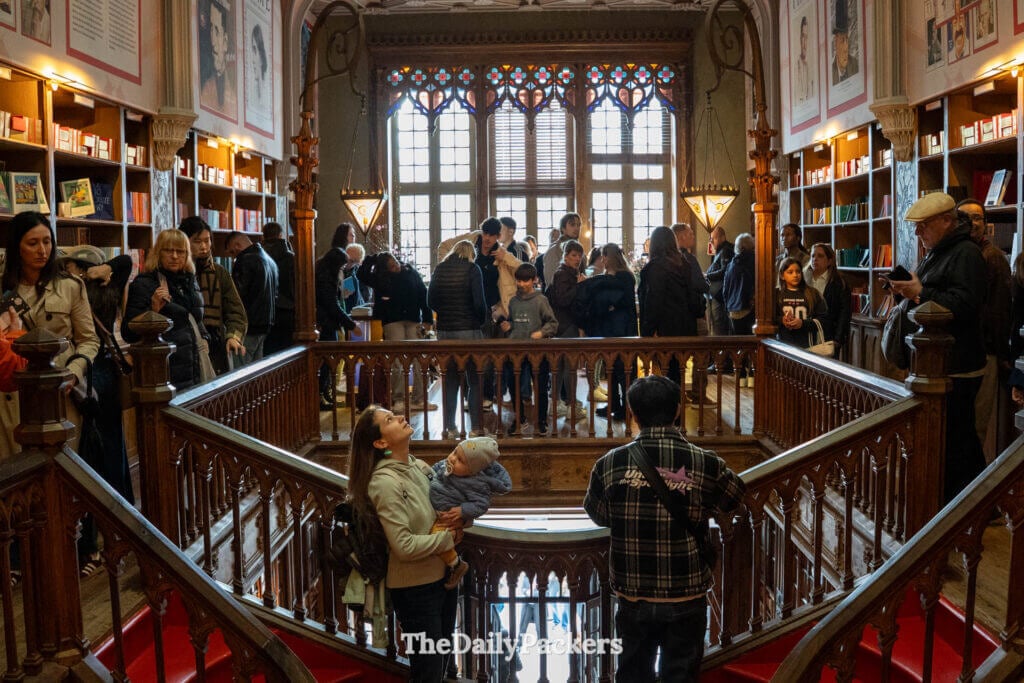 Les visiteurs explorent l'étage supérieur et l'emblématique escalier rouge de la Livraria Lello néo-gothique.