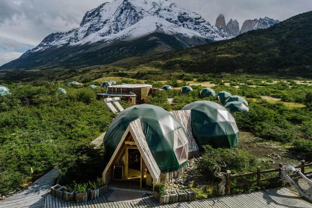Aerial view of EcoCamp Patagonia with iconic green domes set against snowy mountain peaks in Chile.