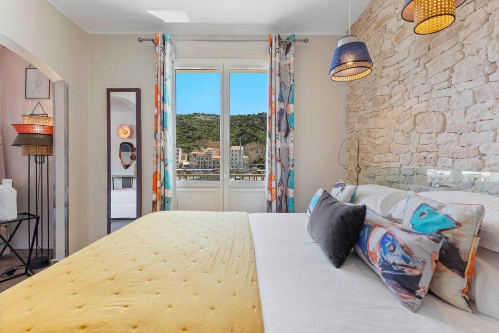 Bright hotel room at Hotel Solemare in Bonifacio with a view of the marina through large glass doors and a private balcony.