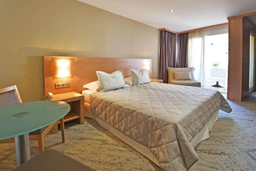 Modern double bedroom at Hotel Le Rocher in Calvi, Corsica, featuring a balcony and wooden accents.
