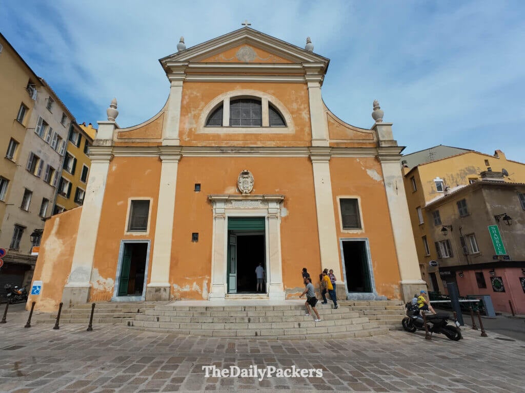The bright orange and cream facade of the historic Ajaccio Cathedral under a blue sky.