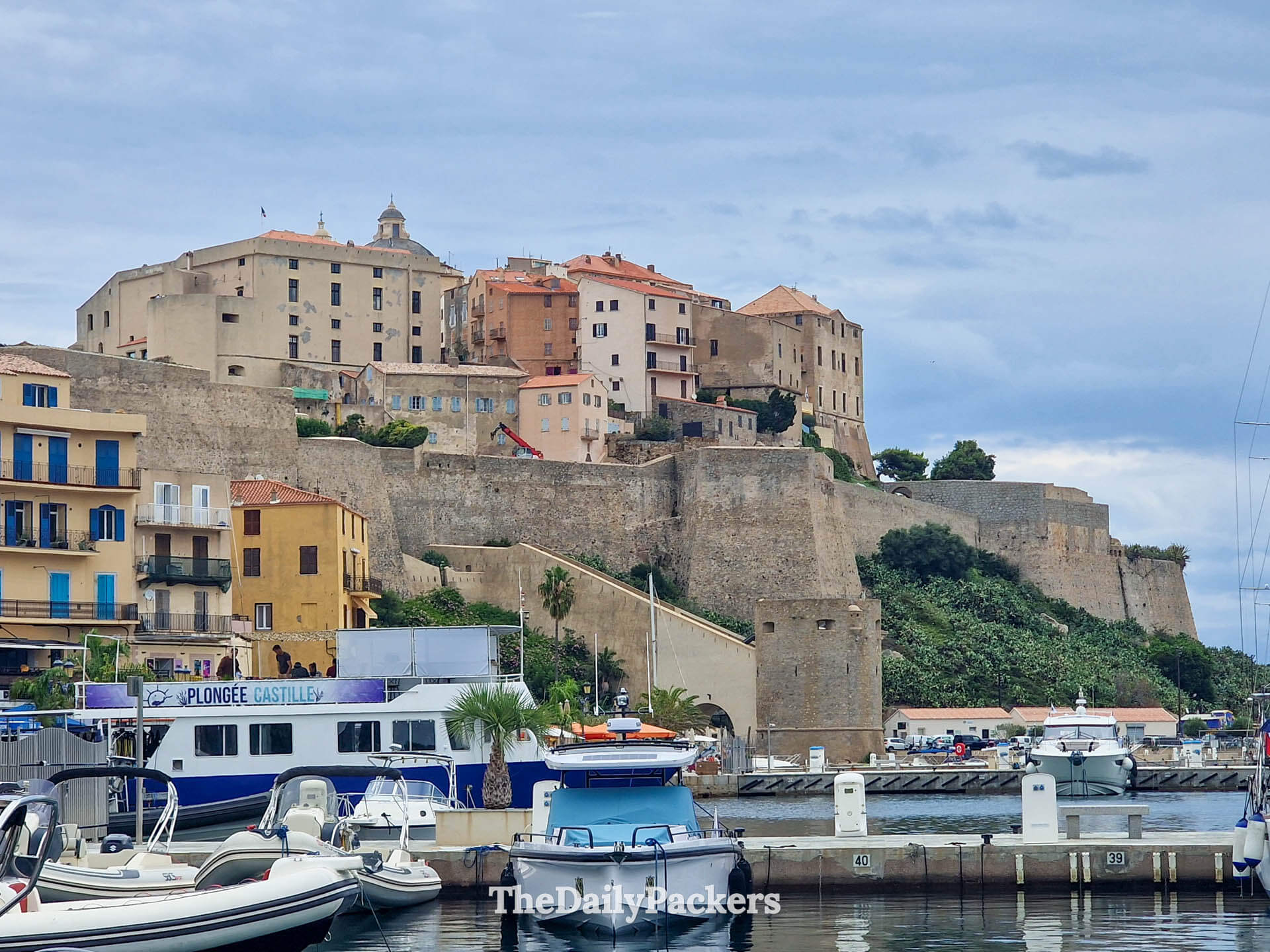 A long view of the mighty medieval stone citadel walls rising above the blue harbor of Calvi.