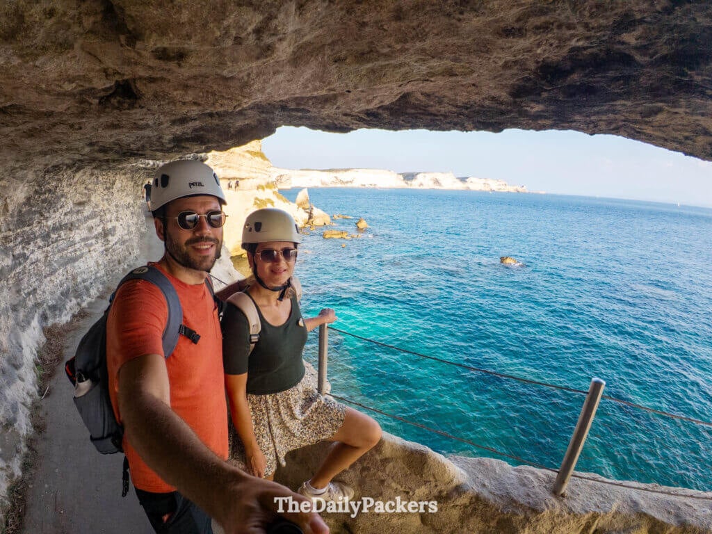A smiling couple wearing safety helmets on the historic King of Aragon Steps in Bonifacio.