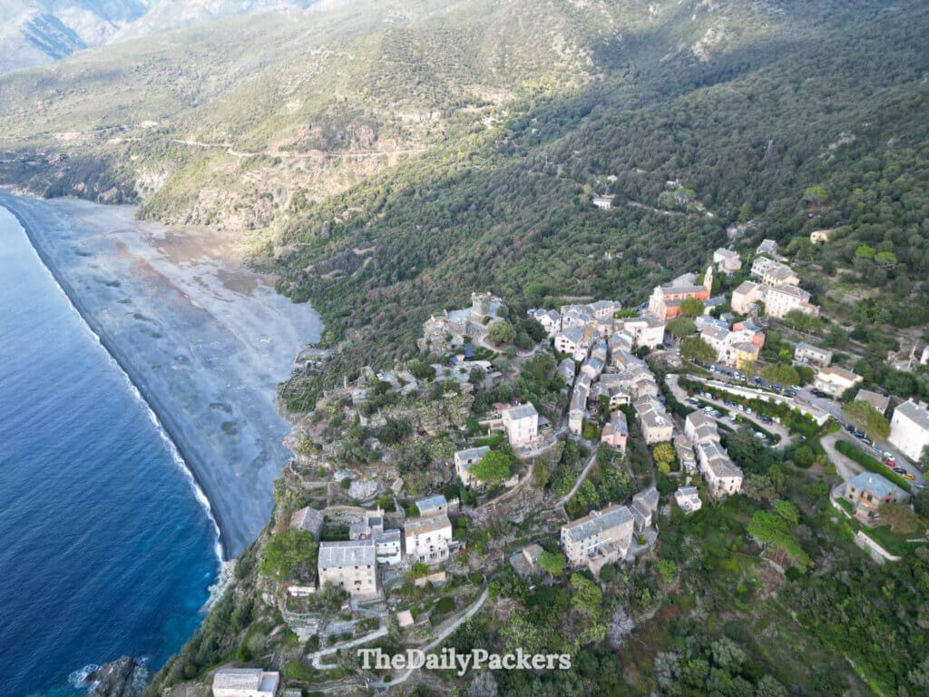Aerial drone view of Nonza village perched high on a steep cliff above the sea in Cap Corse.