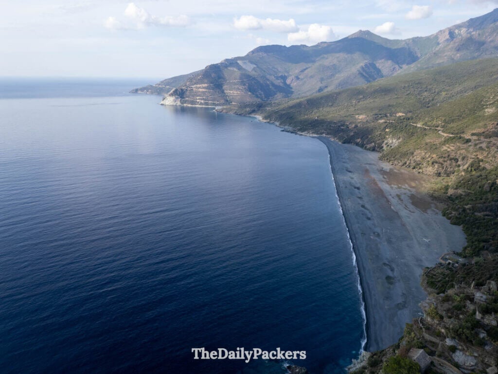The long, dark gray pebble beach of Nonza contrasted against bright turquoise Mediterranean waters.