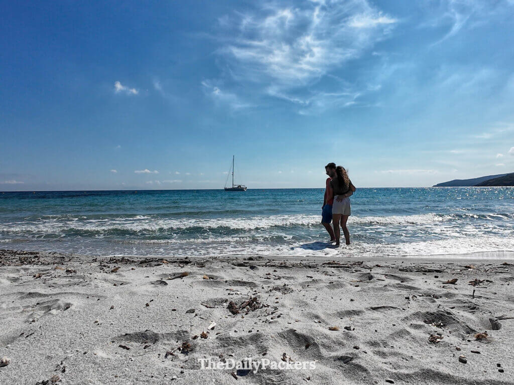 A couple hugging in the blue water at Tamarone Beach, Corsica.