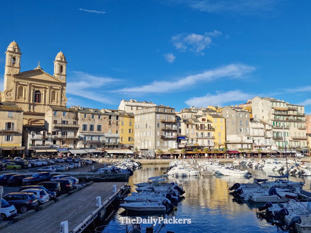 Boats moored in the Vieux Port of Bastia, Corsica, with historic buildings and a church behind.