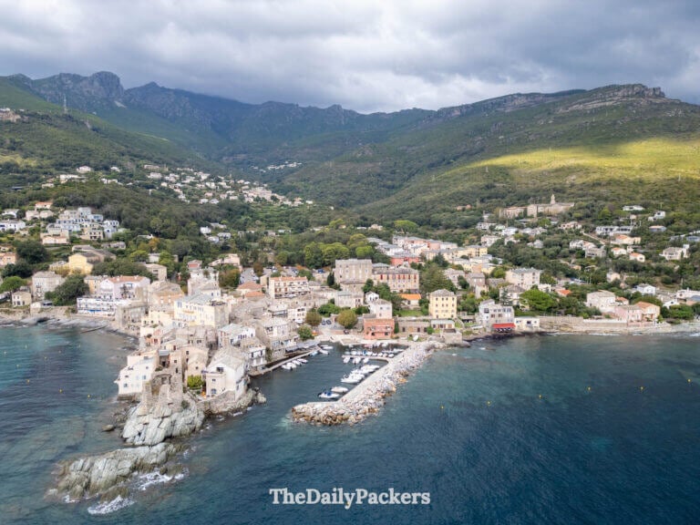 Aerial drone view of the coastal village of Erbalunga, Corsica, nestled against green mountains.