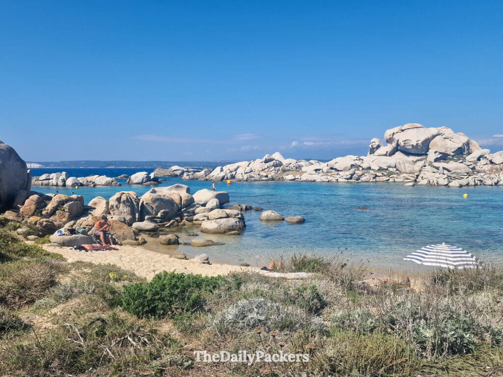 A rocky pathway leading down to the shallow, transparent waters of Chiesa Beach in Corsica