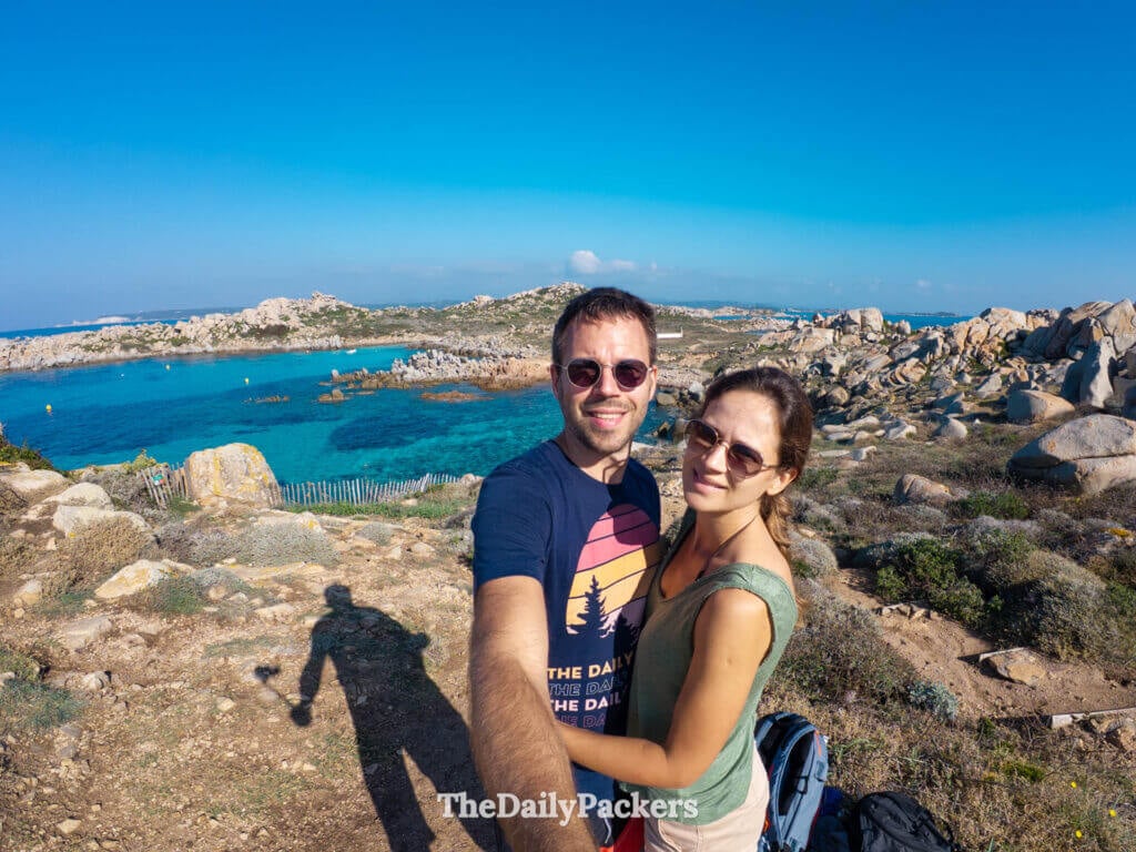 A couple smiling for a selfie with the turquoise sea and rocky shores of Lavezzi Island behind