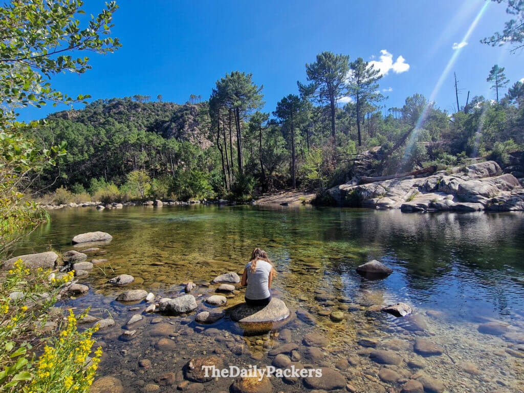 A hiker standing near a natural emerald swimming rock pool in the Solenzara Valley, Corsica.