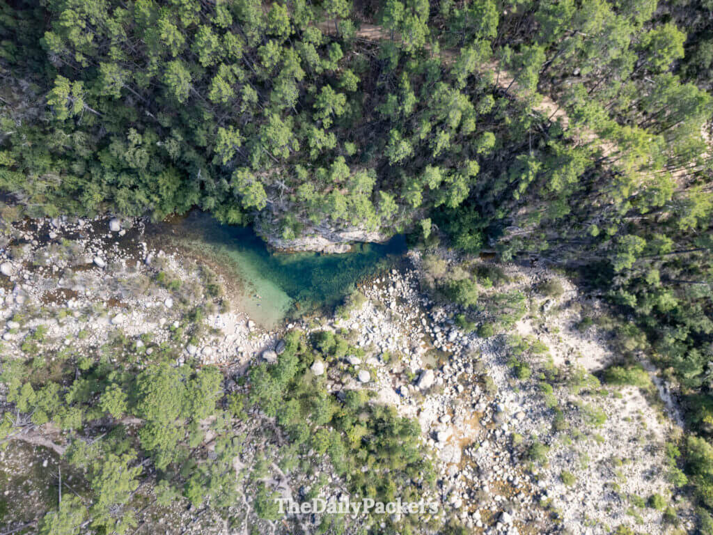 High aerial perspective of a winding river cutting through the forested Solenzara Valley hills.