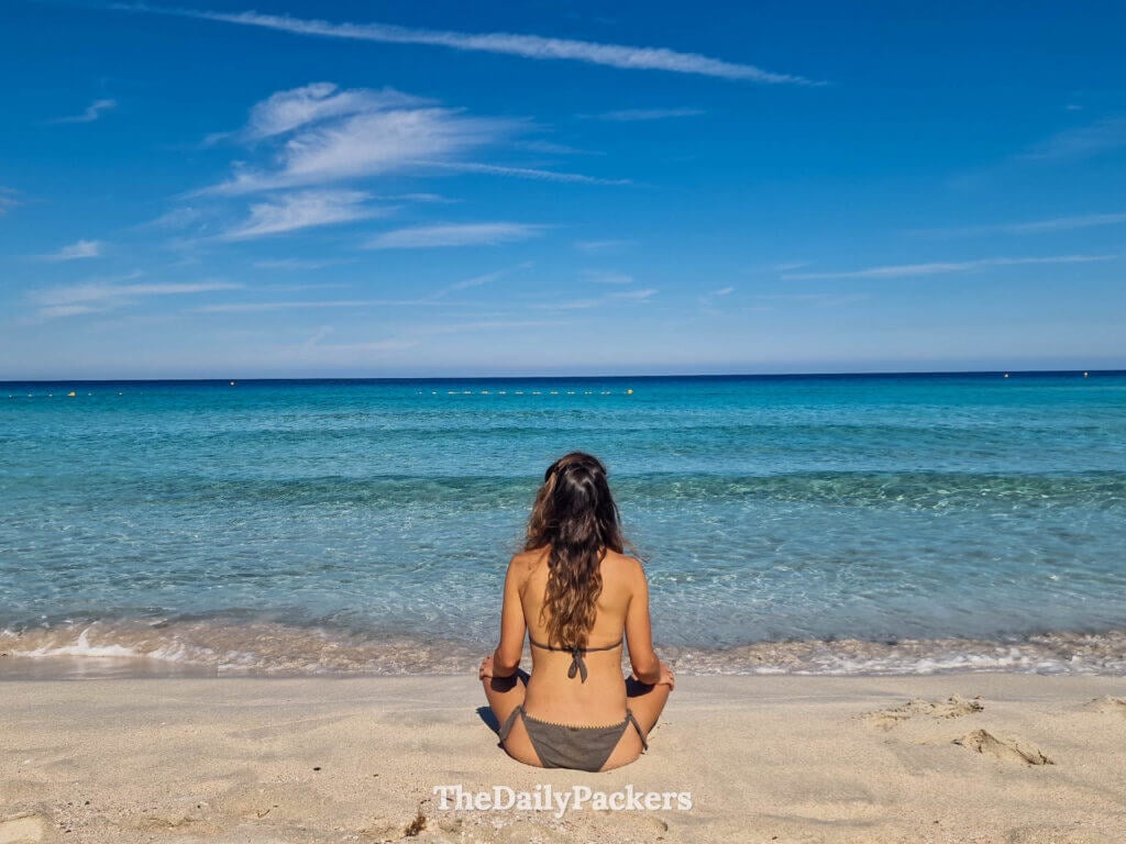 Une femme méditant sur le sable de la plage de Saleccia en Corse.