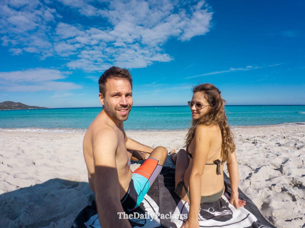 Un couple assis ensemble sur le sable blanc de la plage de Saleccia regardant l’eau cristalline.