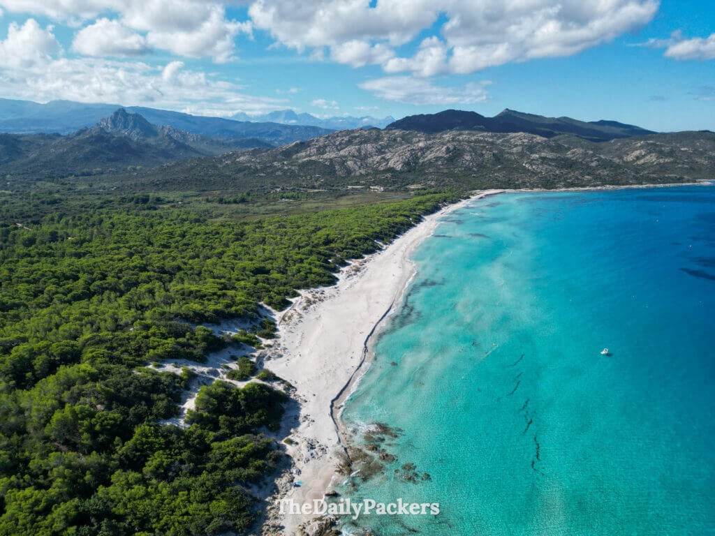 A high-angle drone shot of the turquoise waters of Saleccia Beach with mountains in the background