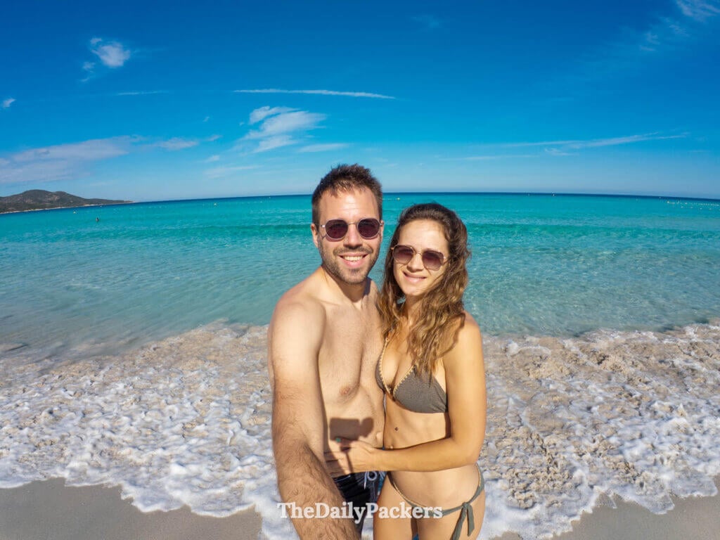 A smiling couple in bikini taking a selfie on the shore of Saleccia Beach in Corsica.