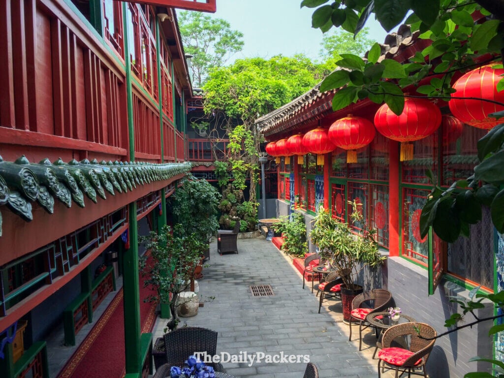 Cour d’un hôtel traditionnel dans un hutong de Pékin, décorée de lanternes rouges et de verdure luxuriante
