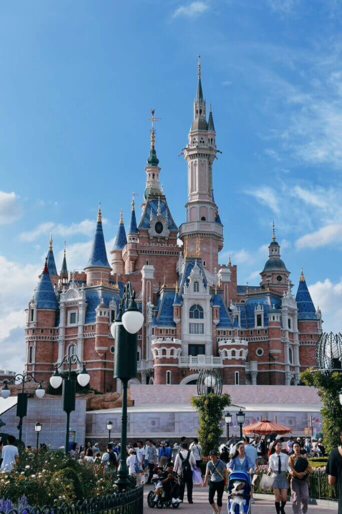 Capturez la magie du château emblématique de Shanghai Disneyland avec des visiteurs profitant d'une journée d'aventure ensoleillée.