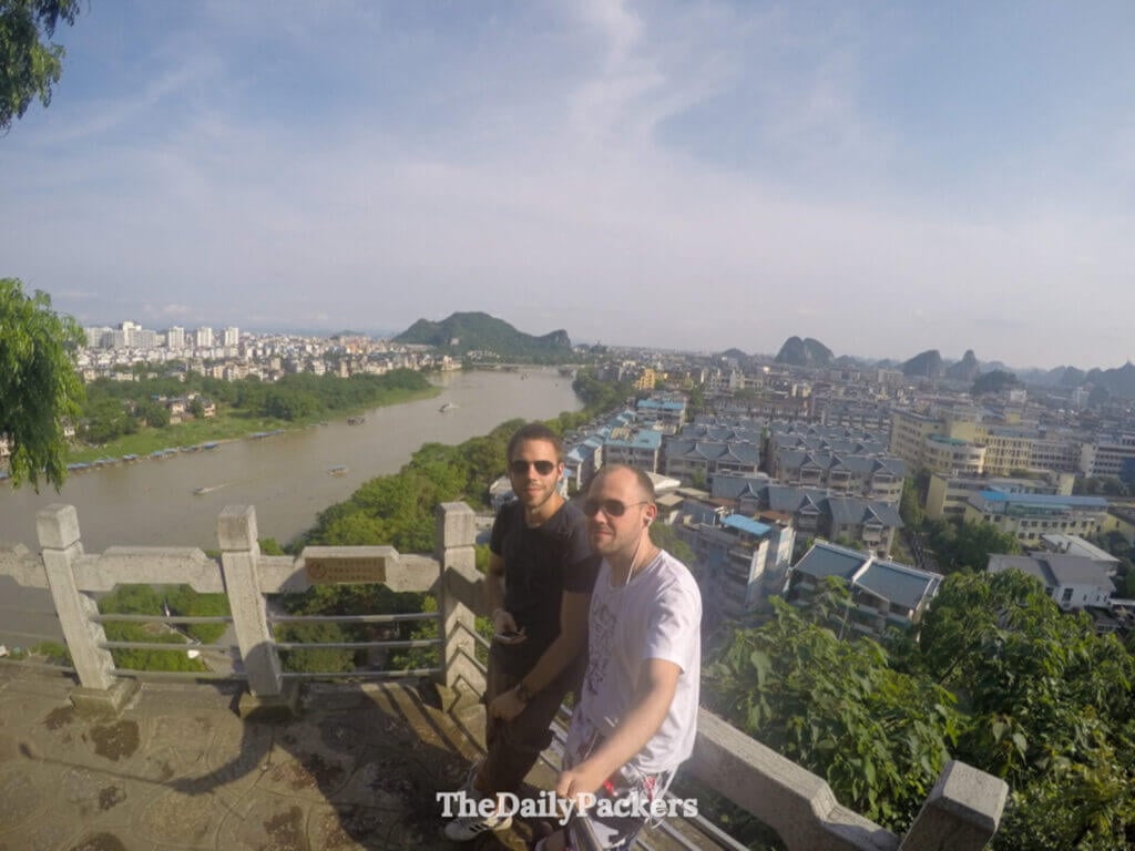 Friends pose by the Li River with Guilin's rooftops and karst hills behind.