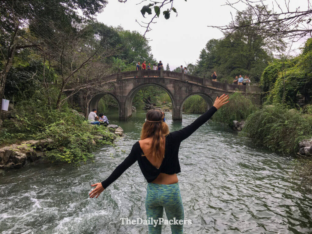 Femme, bras écartés, devant un pont en arche de pierre au-dessus des 18 ruisseaux de Jiuxi, Hangzhou