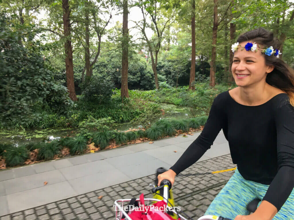 Femme à vélo avec une couronne de fleurs le long d’un joli chemin bordé d’arbres près du lac de l’Ouest, Hangzhou