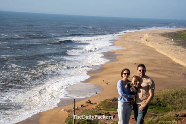 Family of three standing at a scenic cliff viewpoint overlooking Praia do Norte.