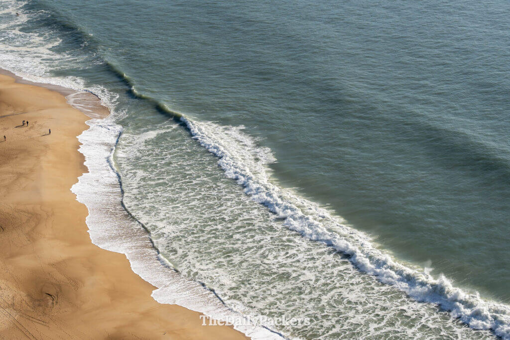 Overhead view of ocean waves breaking on the golden sand of Praia do Nazare in Nazaré, Portugal.