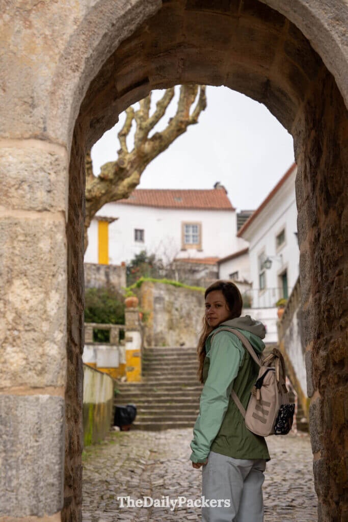 A tourist looks back while walking through a stone archway gate in Obidos, Portugal.