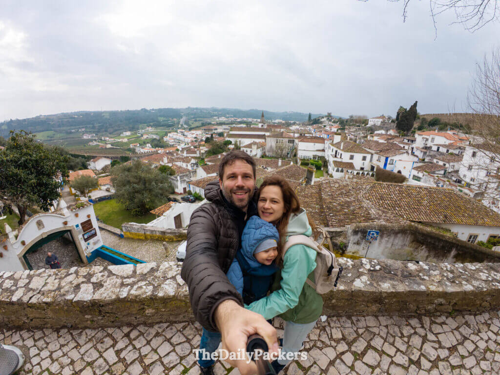 A family takes a selfie overlooking the white houses and tiled roofs of Obidos village.