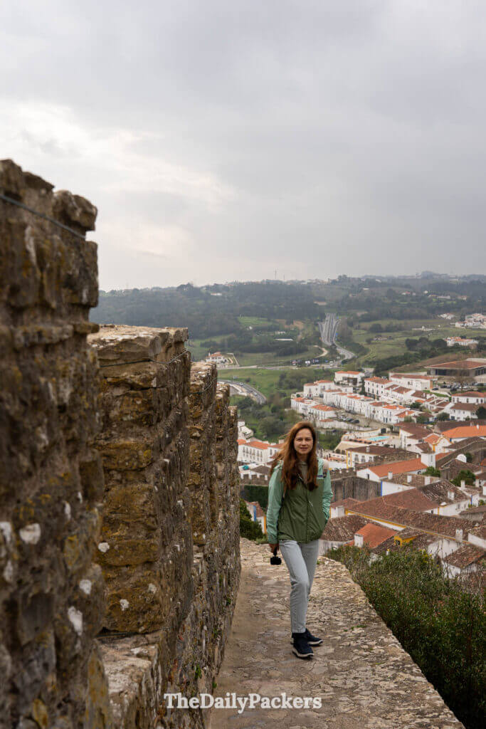 A woman walks along the narrow stone ramparts of the medieval town wall in Obidos.