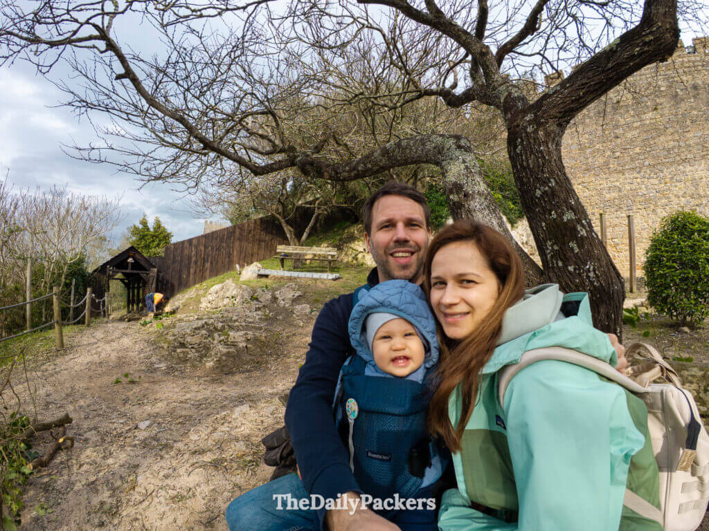 A family smiles for a selfie under a tree outside the stone walls of Porta Talhada.