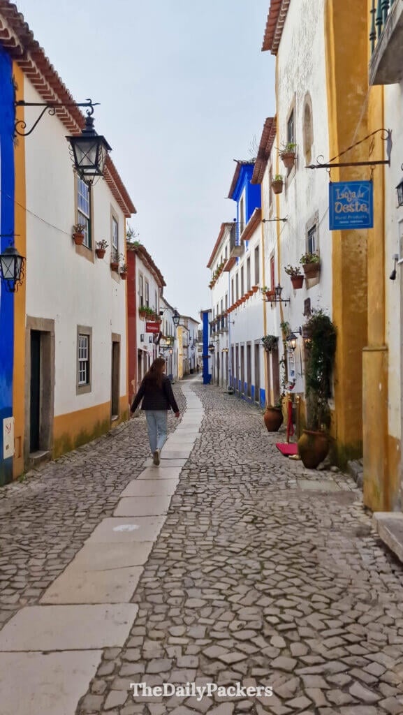Traveler walking along an empty, traditional cobblestone path on Rua Direita in Óbidos.
