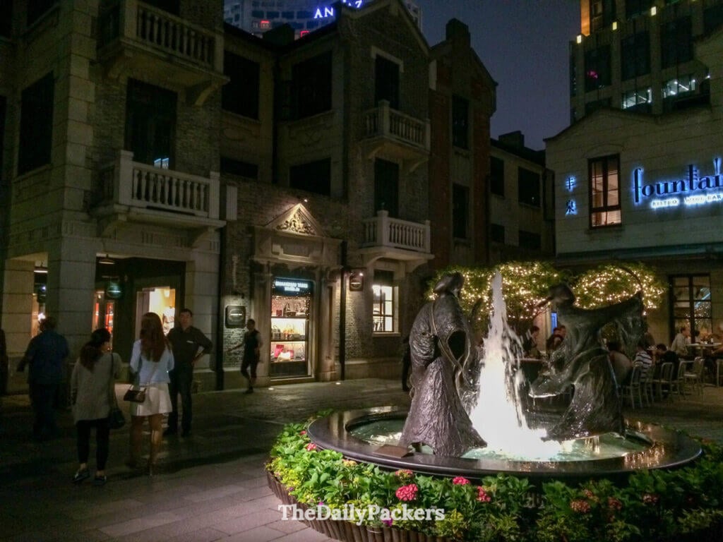 Sculpture de fontaine illuminée dans une cour pavée entourée de bâtiments patrimoniaux restaurés, concession française Shanghai