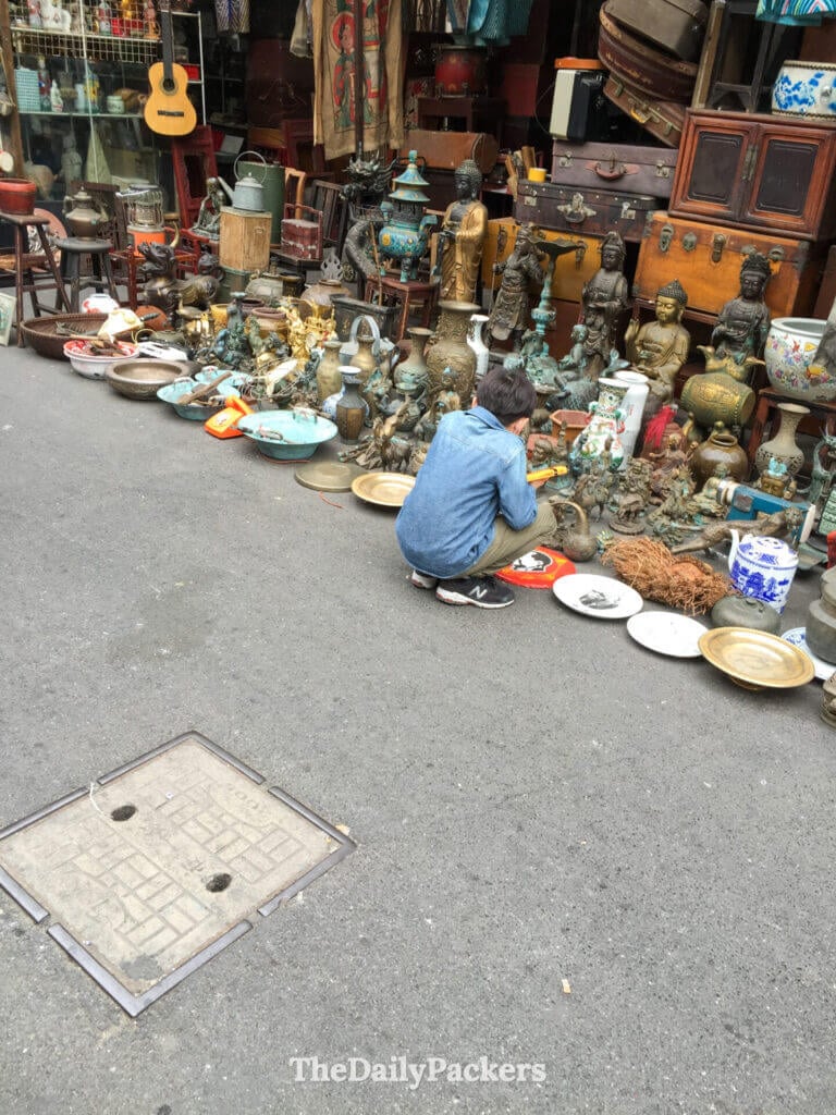 Vendeur parcourant des statues en bronze et des objets vintage étalés le long du marché d'antiquités de la rue Dongtai, Shanghai