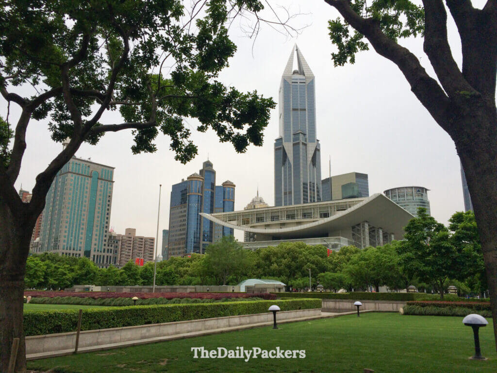 Pelouses vertes et allées bordées d'arbres du parc du Peuple avec le Grand Théâtre de Shanghai et les tours de la ville derrière