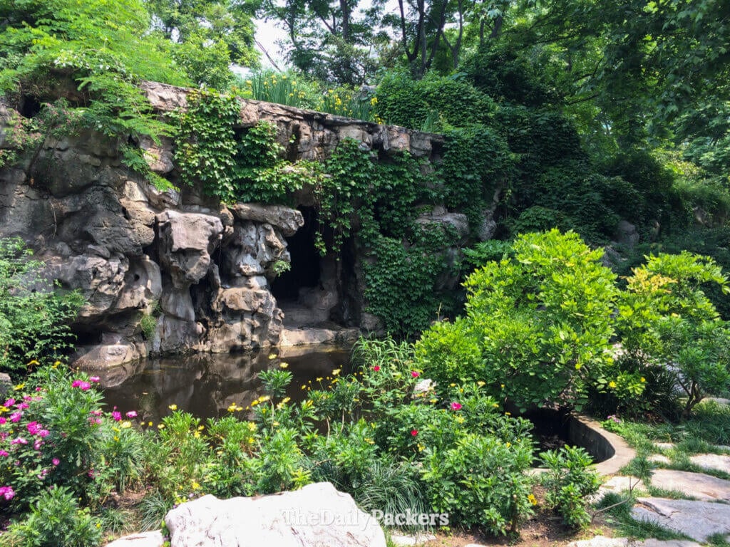 Grotte de rocaille couverte de lierre avec un étang et des fleurs en fleurs dans le parc Jing'an, Shanghai